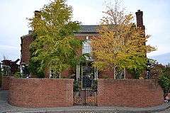 Photograph of a two-story brick house surrounded by a brick wall with rounded corners.