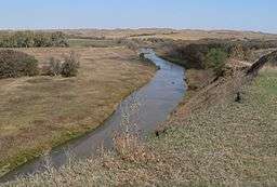 River running through hilly grassland with scattered patches of woodland