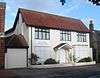 A converted house whose downstairs windows and entrance door are covered with white-painted panels. The three upper-storey windows are glazed and have brown frames.  An entrance porch is carried on spindly columns.