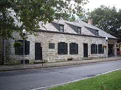 A one-story stone house with black trim and two lampposts in front.