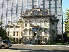 Photograph of the Leland Stanford House, an impressive Victorian with a modern office tower rising behind.