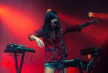 A woman surrounded by keyboards, singing into a microphone.