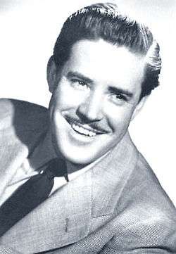 Black-and-white photo of smiling, mustachioed man in a suit