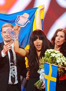 A picture of a woman on a stage holding a microphone shaped trophy in her right hand.