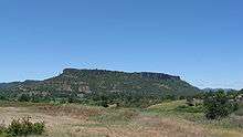 Lower Table Rock from across a field. Similar to Upper Table Rock, it rises steeply to its very flat top.