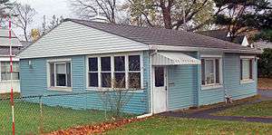 A small one-story blue house with clapboard siding and a gently-sloped gabled roof