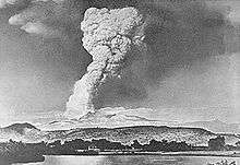 Mushroom-shaped cloud with long neck above a line of ridges.