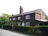 Cottages in two storeys by the road behind a hedge, with a single tall central chimney.