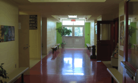 "A front view of a corridor with red tiles and four benches, with a door at its end."