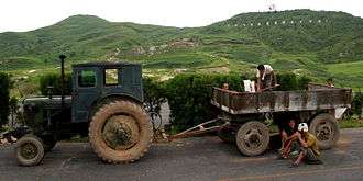 Farmers having a break in front of a tractor's trailer. There are hills on the background.