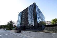 A black glass cubic building with a sidewalk and low retaining wall with "Exelon Pavilions" on it in front.