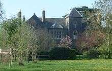 Gray stone building with short tower, partially obscured by trees.