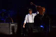 McCartney holding up a guitar on stage.