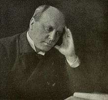 A faded monochrome photograph of a man leaning on a table.