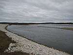 A wide river curves by a rocky shore and across a flat plain.