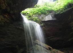 A waterfall pours through a semicircular hole in a rock ledge