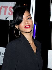 A brunette woman who is wearing a red lipstick and big earrings is smiling