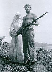 Black and white photo of Robert Mitchum holding a gun standing next to Deborah Kerr in the movie Heaven Knows Mr. Allison in 1957