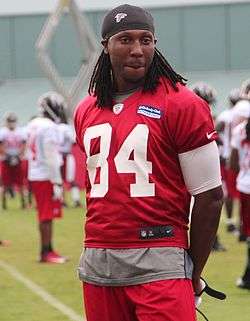 A man wearing a red football jersey and pants with a black hat