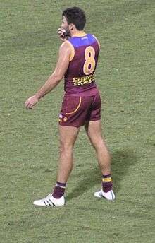 A man in a maroon jersey wearing number 8 stands on grass.