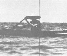 A man wearing a broad straw hat is rowing an outrigger dugout canoe has seen the periscope of the nuclear submarine USS Triton