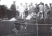 a black and white photograph of the side of a ship hull with a large hole in it