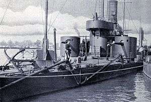 a black and white photograph of a shallow draught ship alongside a dock