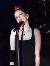 A light-skinned woman with red hair is seen looking up while she sings into her microphone