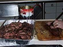 A member of the catering staff slices the pre-cooked beef loin into slices behind the scenes at a beefsteak