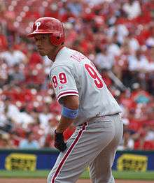 An Asian man wearing a gray baseball uniform with red trim and a red baseball helmet