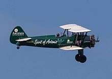 A green biplane with white wings and fixed undercarriage