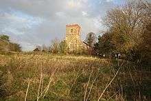 a late summer grassy field, and beyond on the highest ground a greenstone church tower