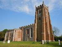 A brick tower with a battlemented parapet, and the body of the flint church beyond it