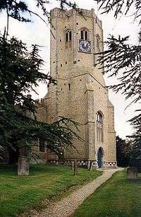 The stone tower of a church with buttresses and an octagonal top stage with a clock