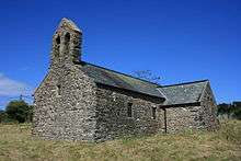 A simple stone church with a slate roof, a bellcote on the nearest gable and a transept on the right