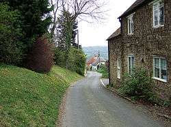 Street scene with a narrow raod with houses on the right and trees on the left.