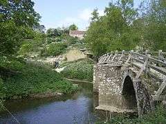 Stone arched bridge with wooden handrail over river.