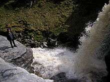 Foamy water falling from high about 10m into turbulent water pool framed by rocks