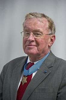 Head of a white man in a suit with a medal hanging from a blue ribbon around his neck