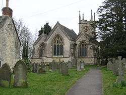 Gray three bay building with arched windows. Tower behind and gravestones in the foreground.