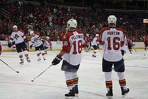 Two hockey players stand on the ice during pregame warm-up with their backs to the camera