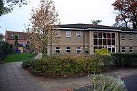 A large modern building with a plate glass central window. Behind it is a red house.