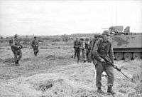 A black and white image of New Zealand soldiers and an armoured personnel carrier during Operation Coburg