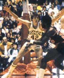 A man wearing a white jersey with the word "SONICS" and number "42" written on the front spreads his arms in a defensive position.